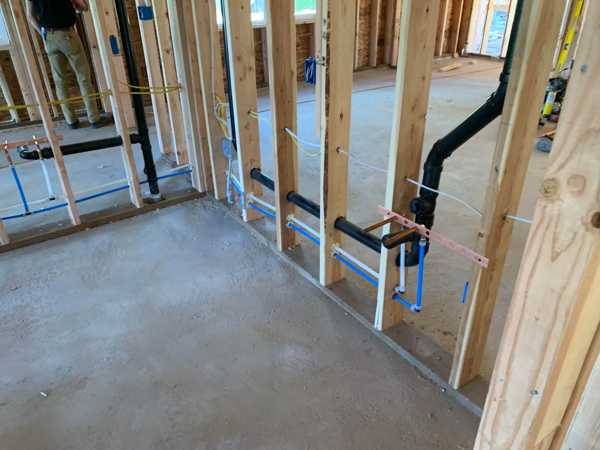 Framing of a bathroom under construction, showing plumbing and electrical wiring within the wooden walls.