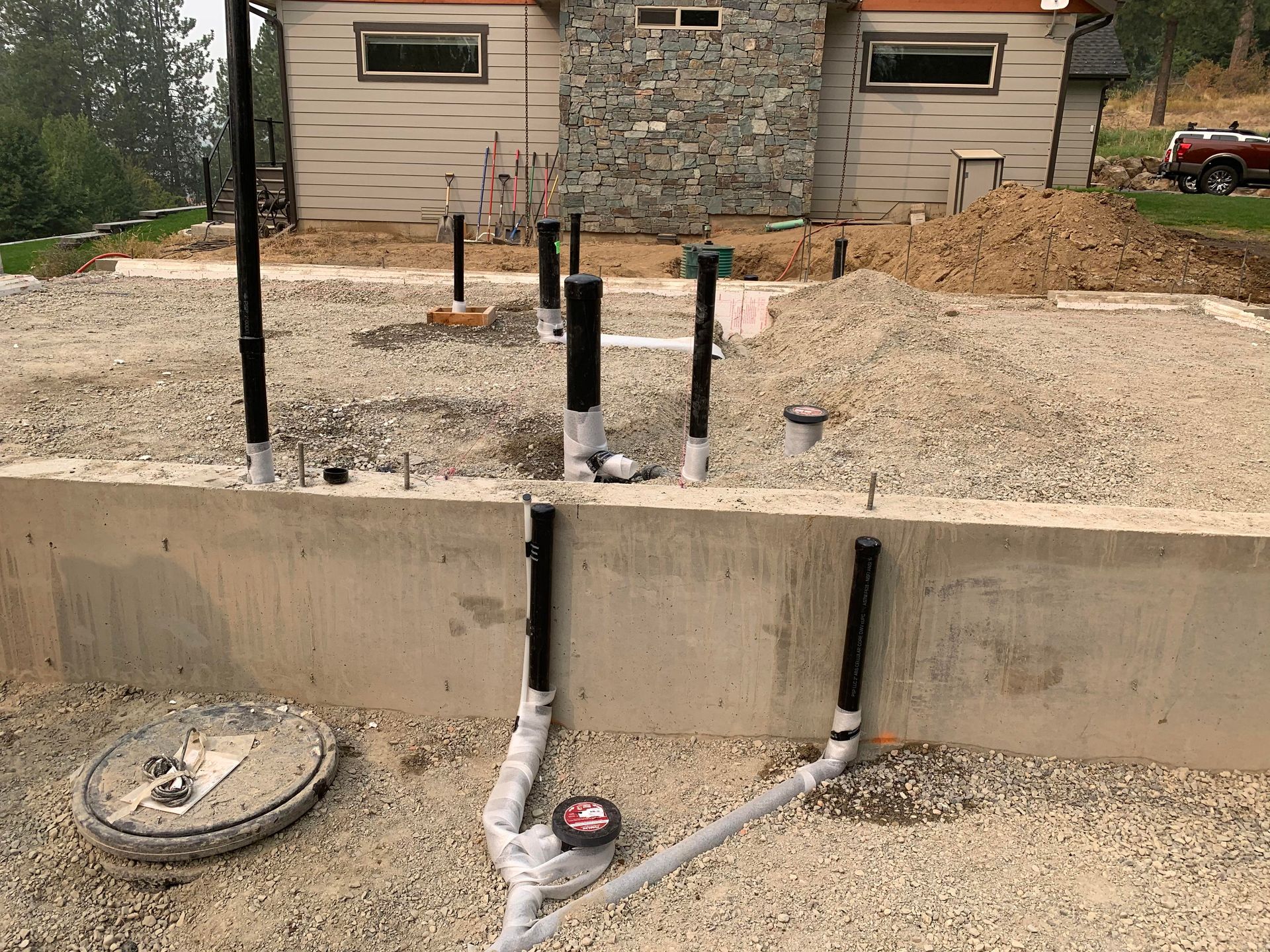 Plumbing pipes emerging from a concrete foundation, gravel bed in a construction site.