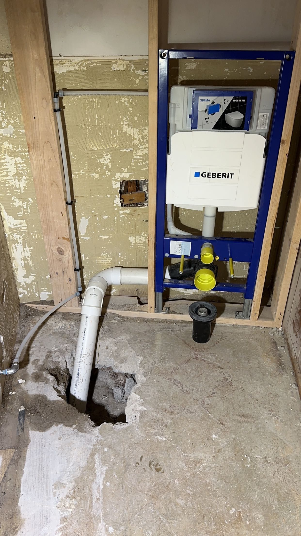 Toilet plumbing rough-in with a Geberit tank and drainage pipe exposed in a bathroom during renovation.