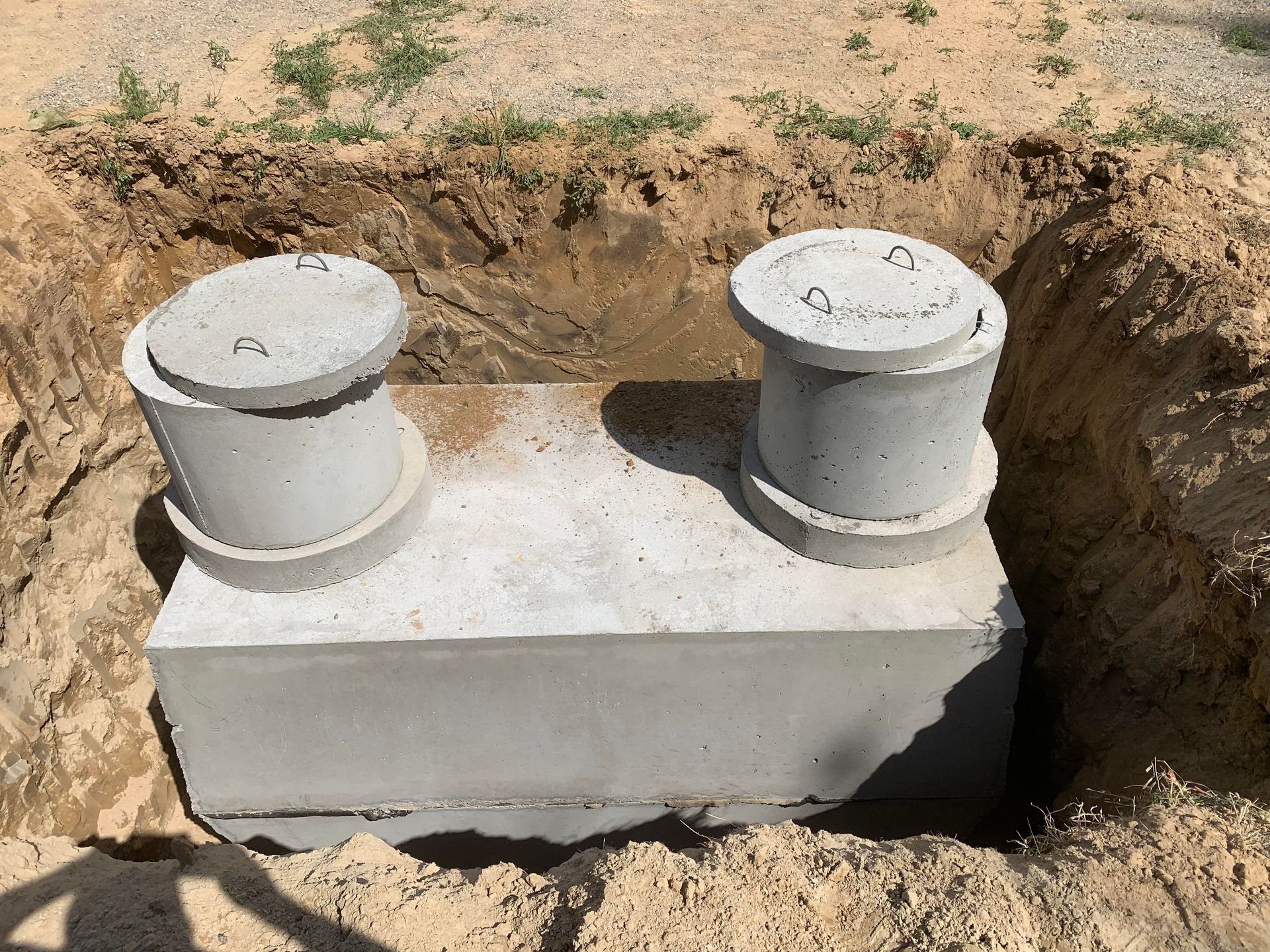 A concrete septic tank with two access points sits in an excavated pit.