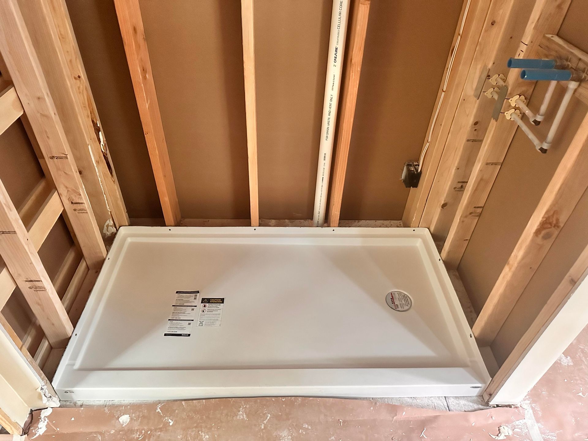 Framed bathroom shower base within wooden studs, plumbing visible.