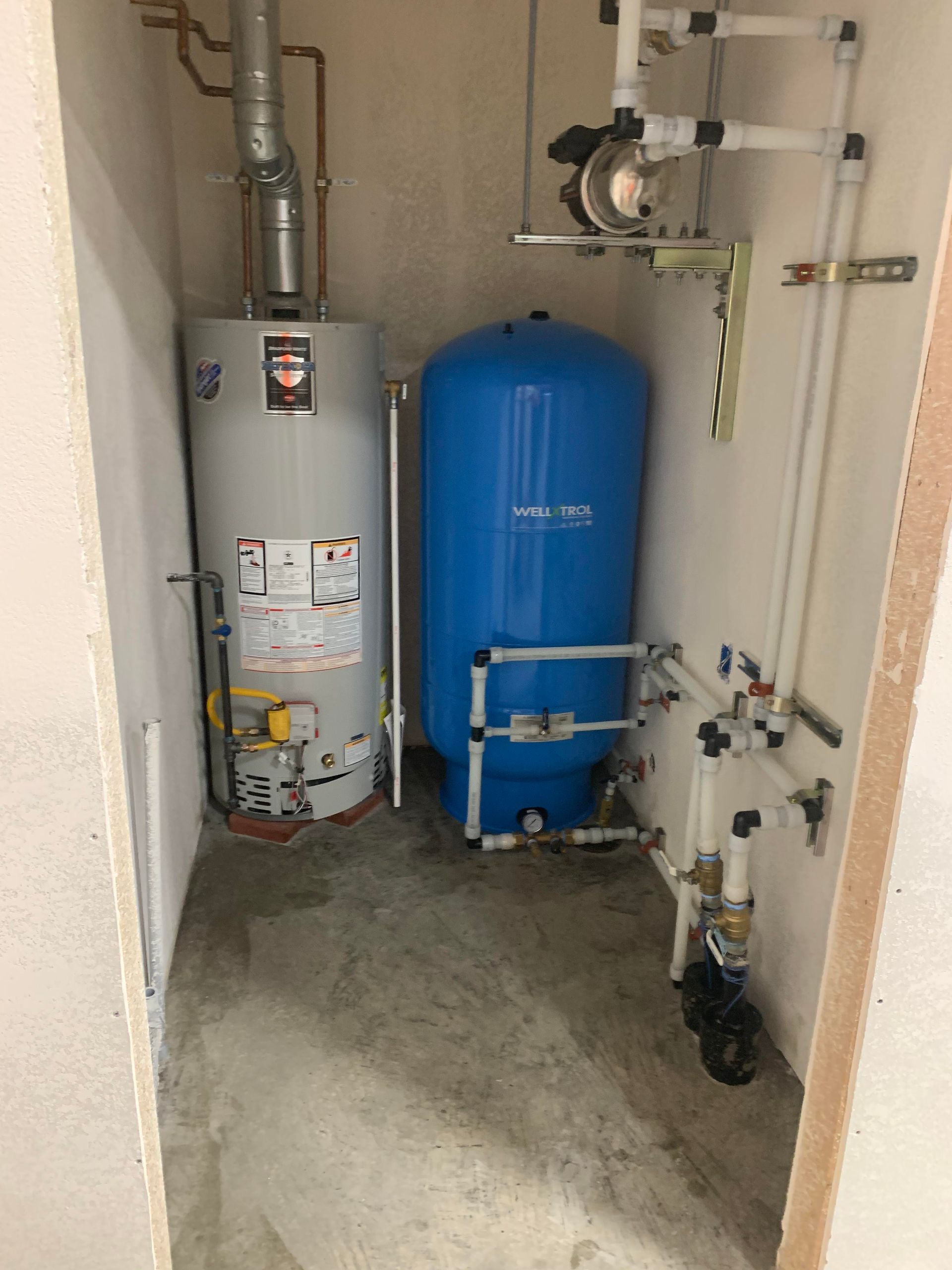 Water heater and pressure tank in a utility room. The water heater is gray, the tank blue.