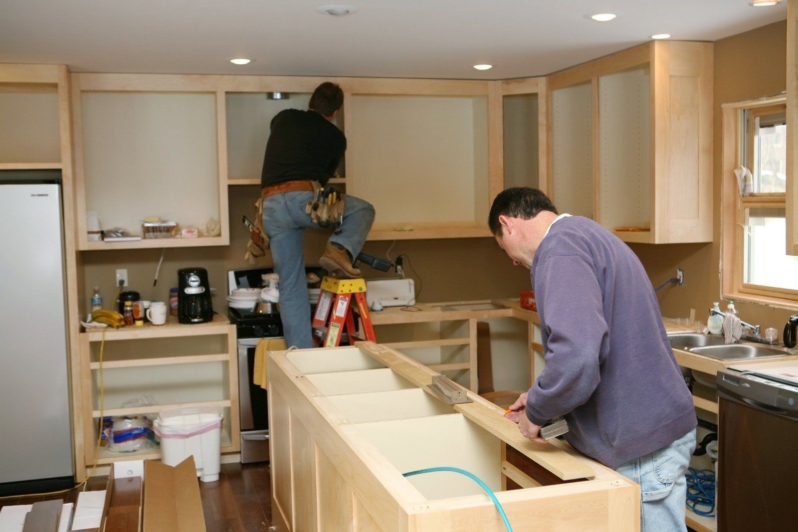 Two men are working on a kitchen with a ladder
