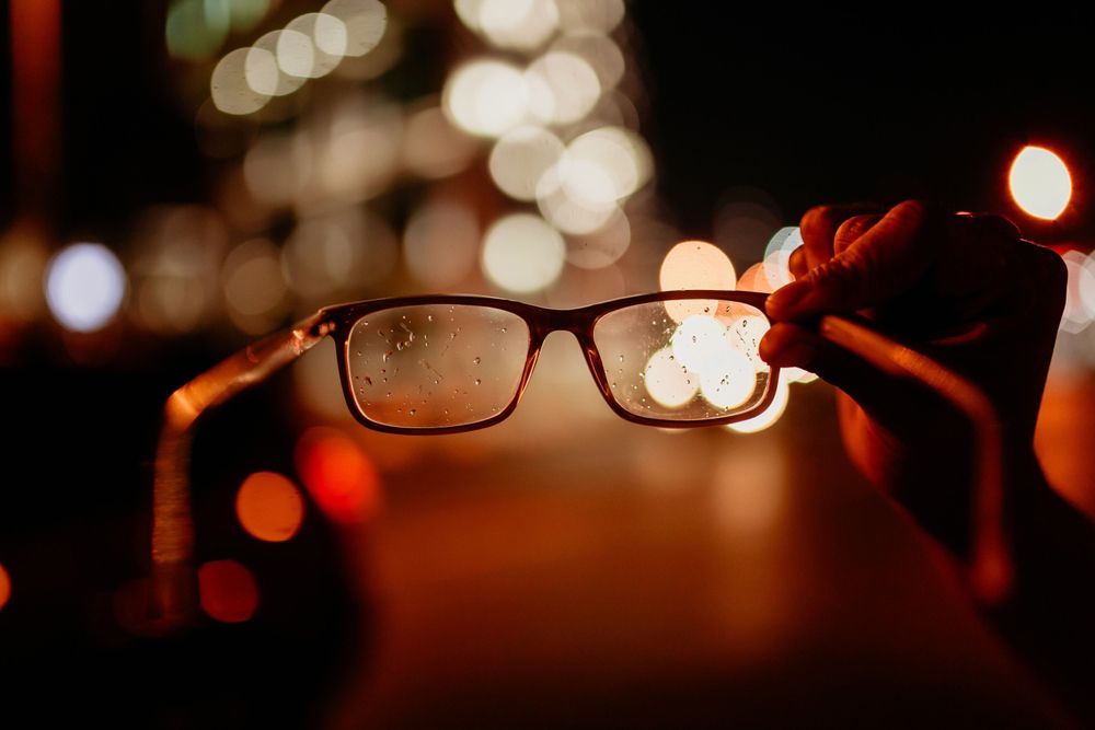 A person is holding a pair of glasses in front of a blurry background