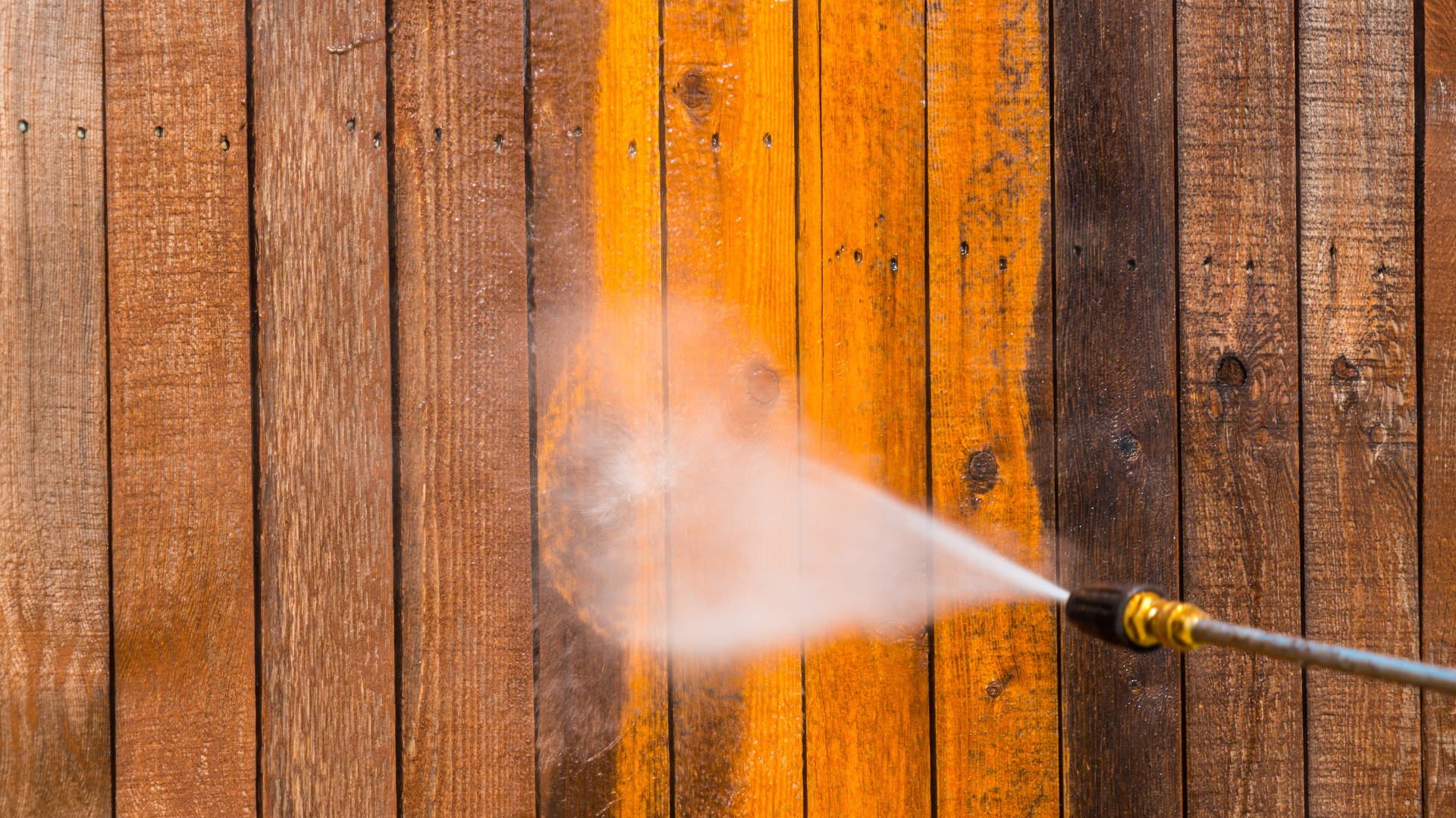 A person is using a high pressure washer to clean a wooden fence