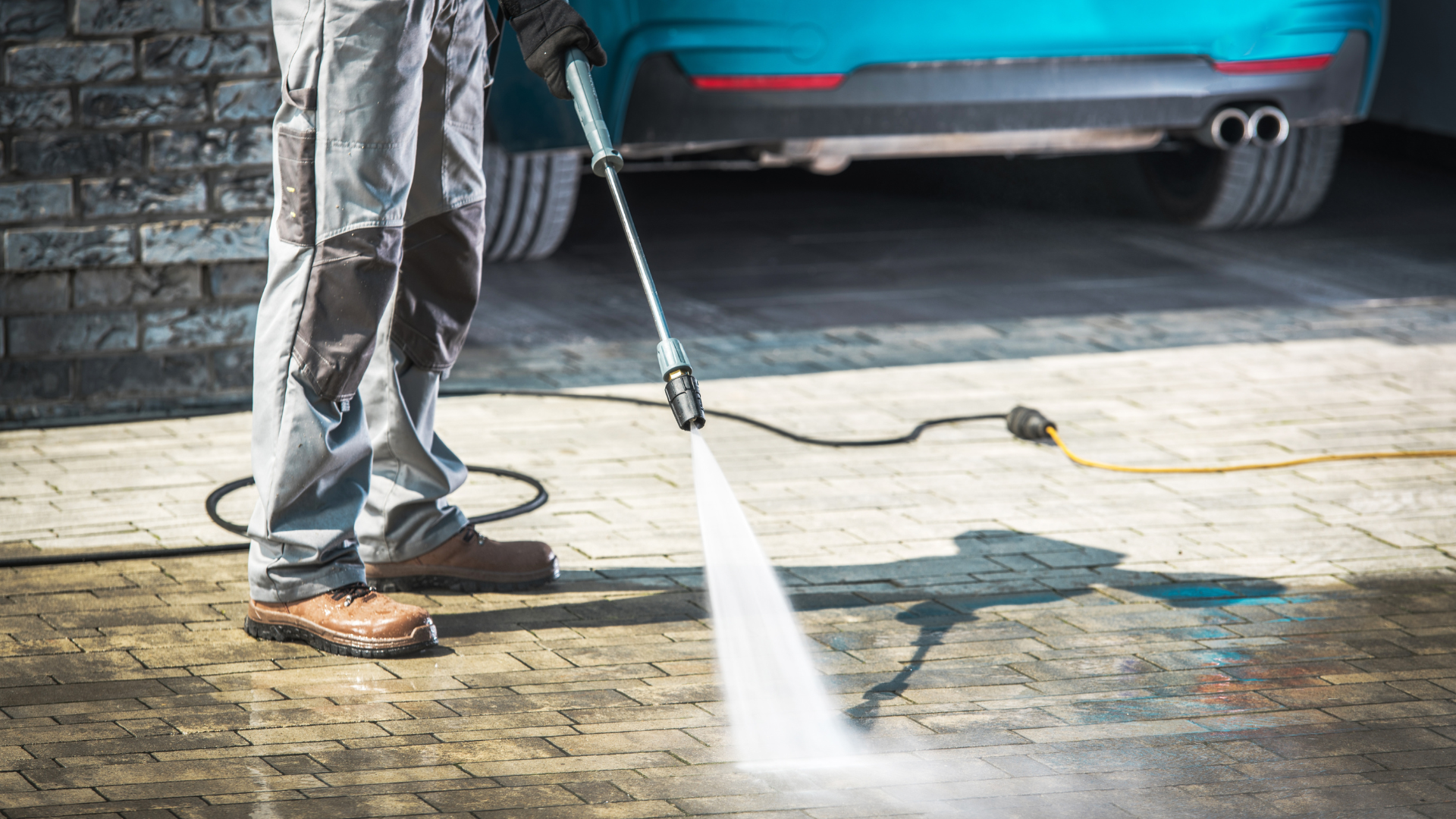 A man is using a high pressure washer to clean a driveway