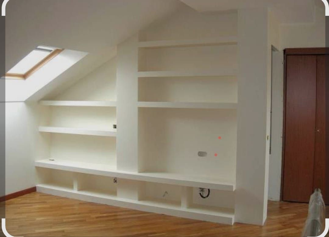 Scaffalature e armadi a muro bianchi in una mansarda inclinata con pavimento in legno e lucernario.