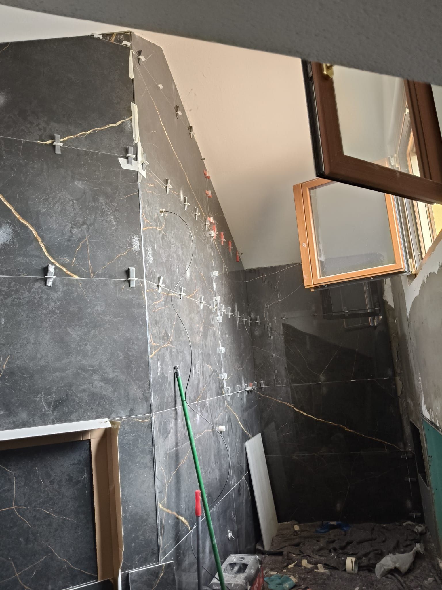 Vano scale parzialmente ristrutturato con pareti scure, intonaco a vista, attrezzi e detriti sul pavimento.