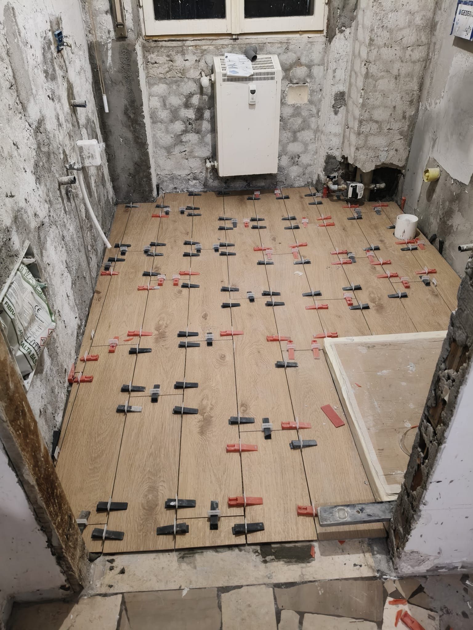 Bagno ristrutturato con pavimento piastrellato non rifinito, WC sospeso bianco e finestra sul retro.