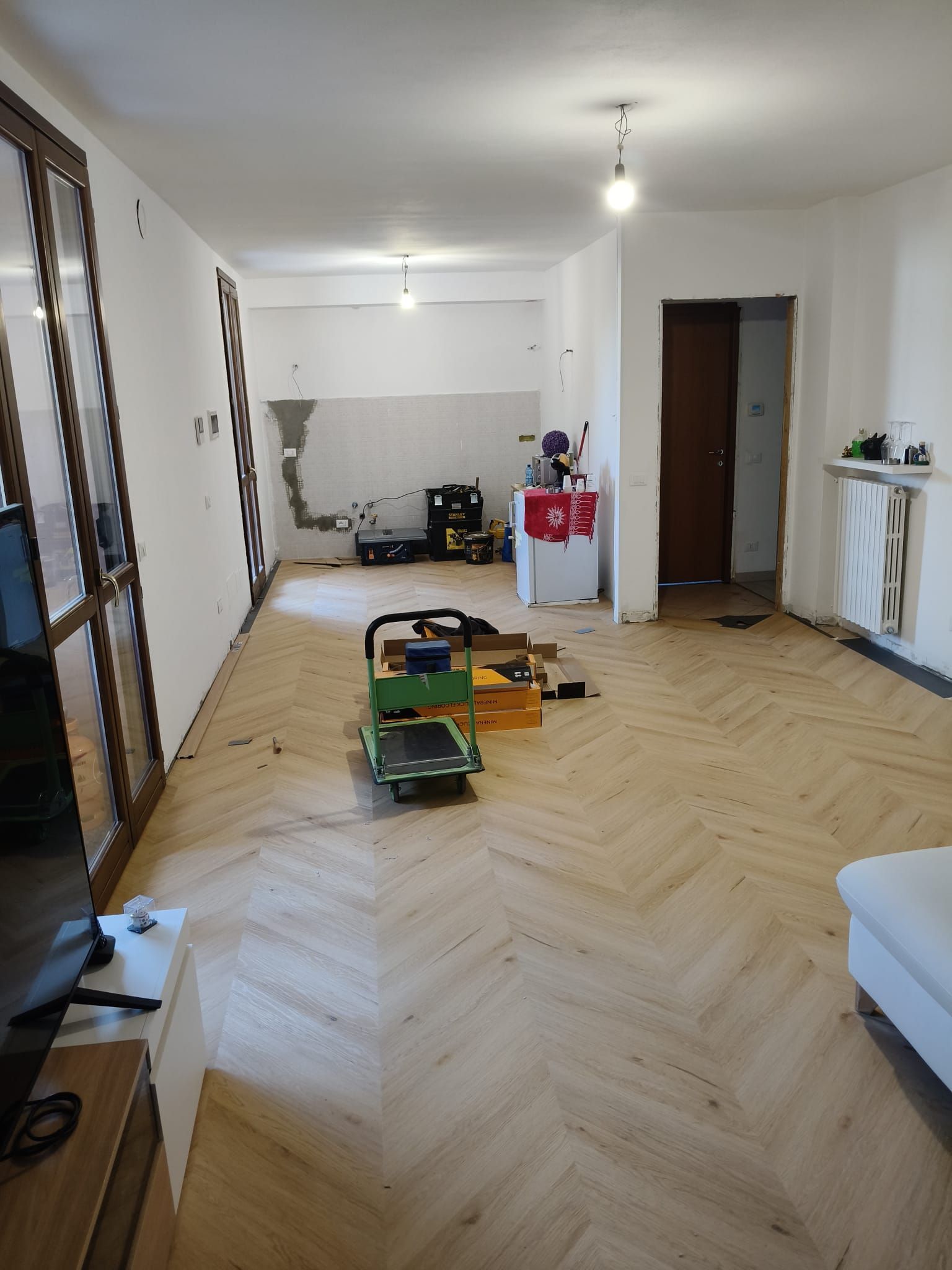 Luminoso soggiorno con pavimento in legno a spina di pesce, giocattoli sparsi e pareti bianche con porta aperta.