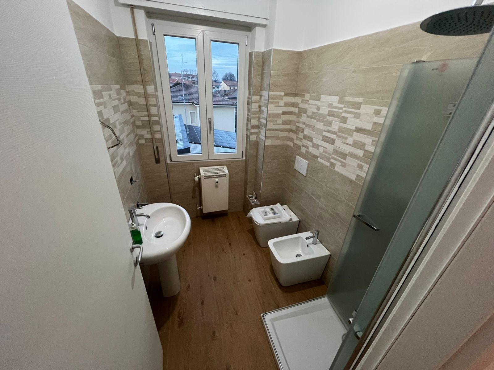 Piccolo bagno con WC, lavandino, bidet, doccia e una finestra in fondo.