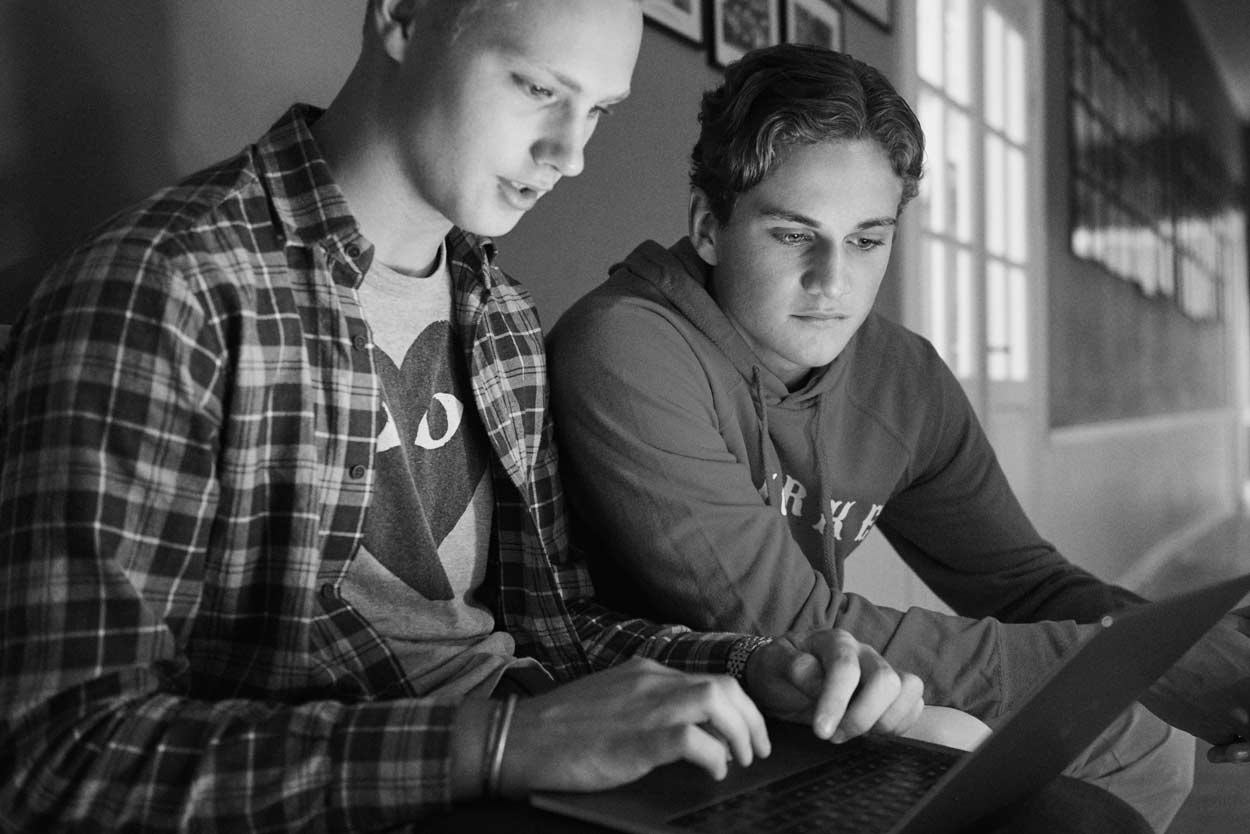 Två unga män sitter vid ett bord och tittar på en bärbar dator.