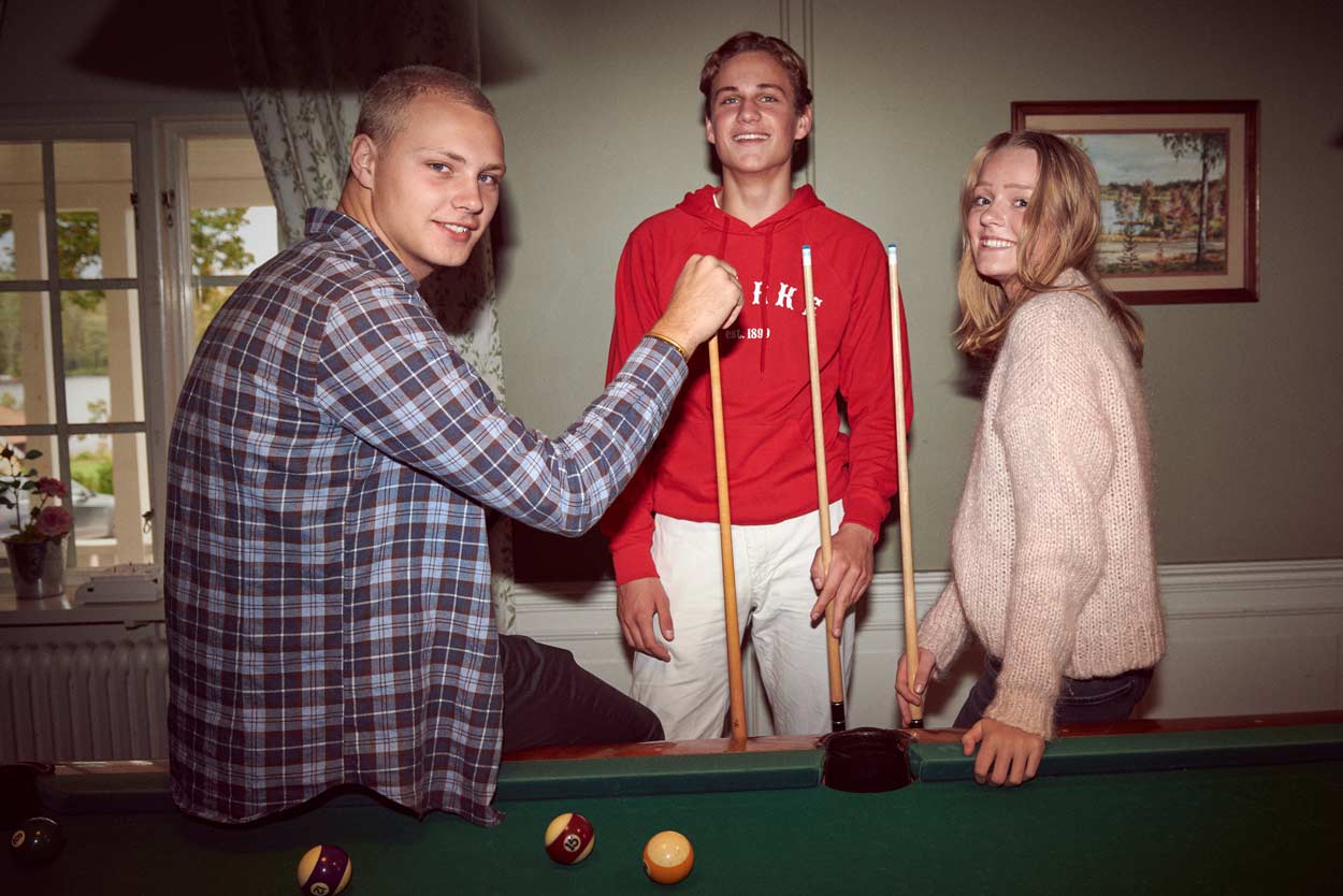 En grupp ungdomar spelar biljard i ett vardagsrum.