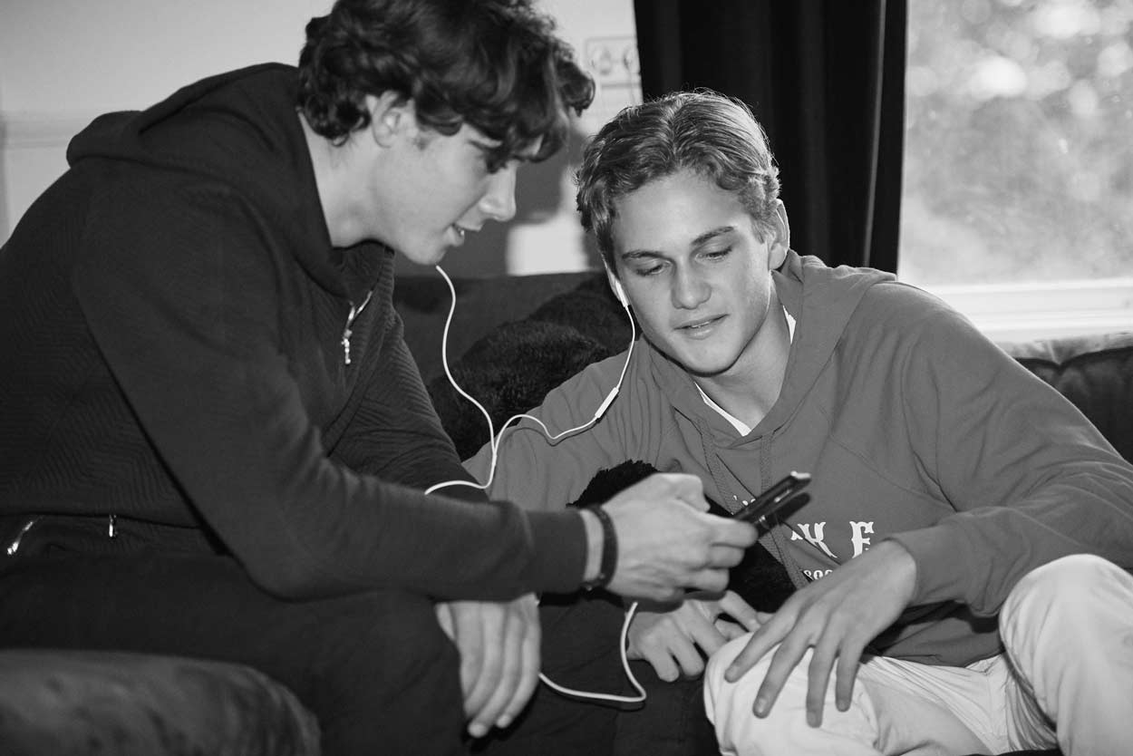 Två unga män sitter i en soffa och tittar på en mobiltelefon.