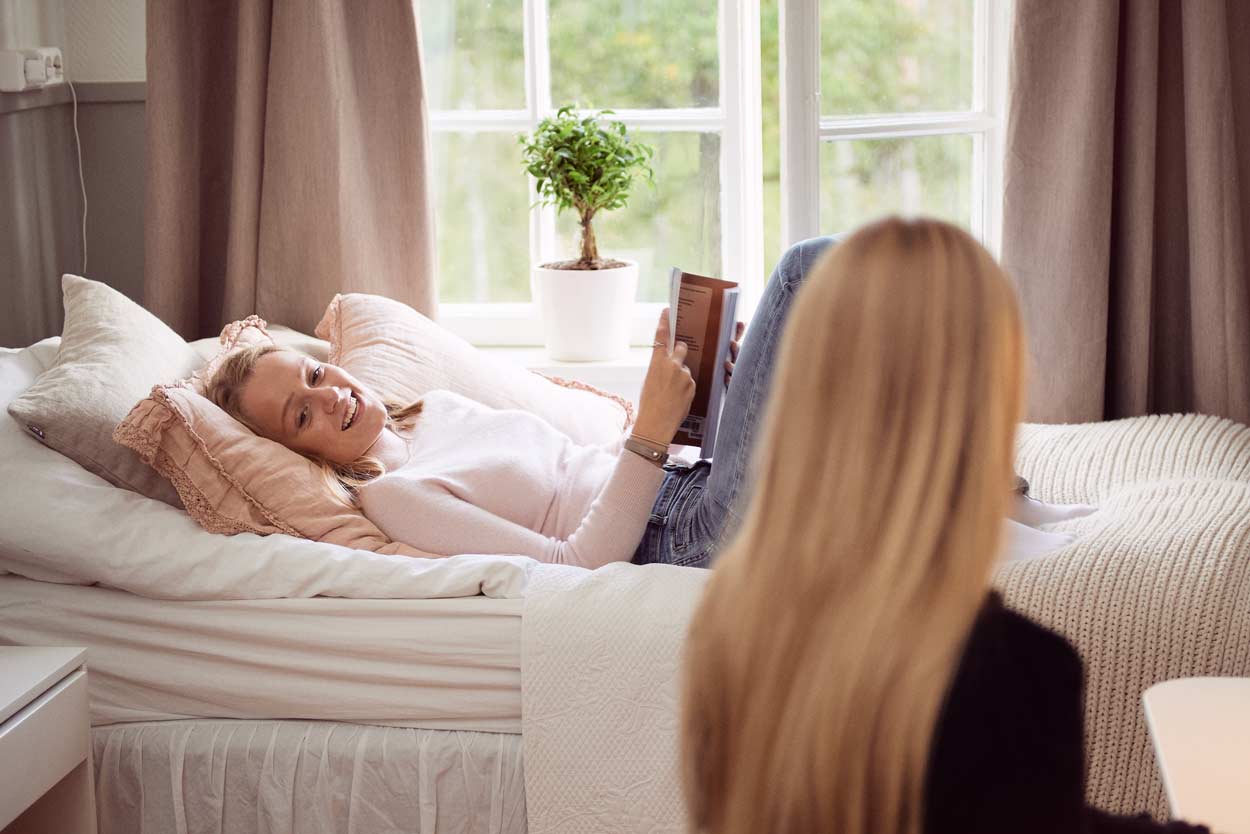 En kvinna ligger på en säng och läser en bok.