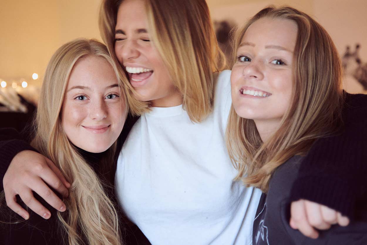 Tre unga kvinnor poserar för en bild tillsammans och ler.