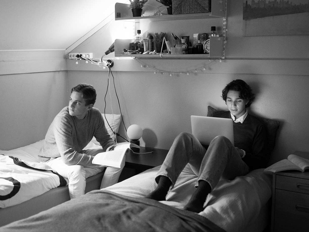 Två män sitter i sängar i ett rum med en bärbar dator.