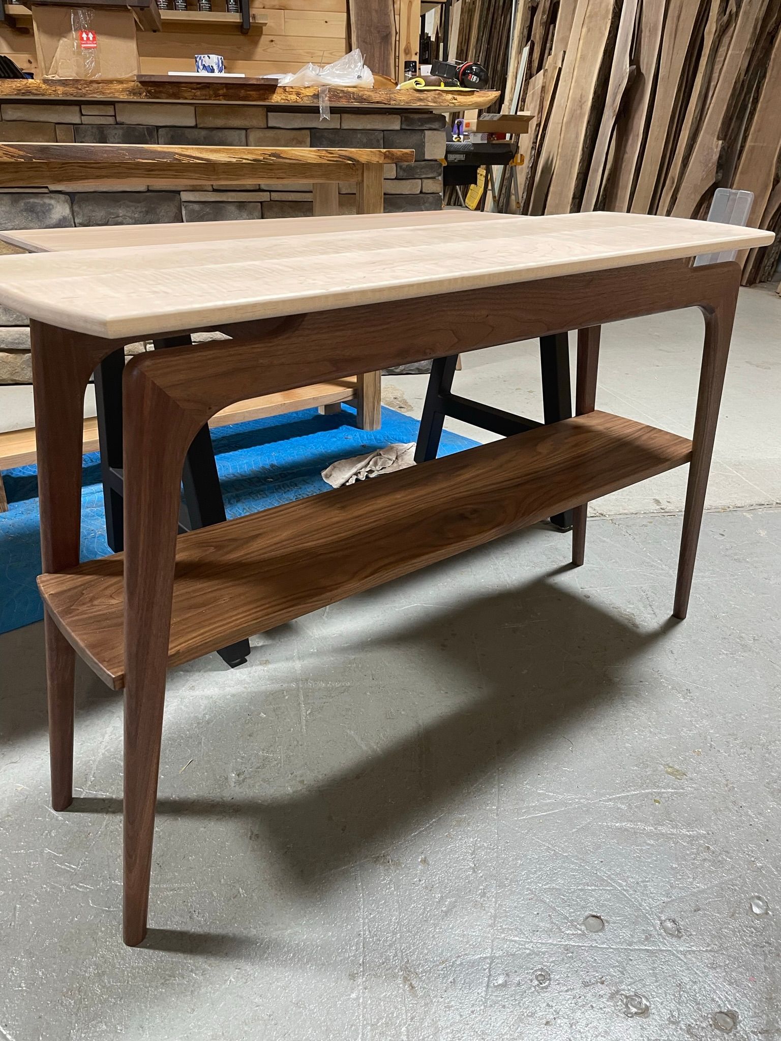 A wooden table with a shelf underneath it is sitting on a concrete floor.