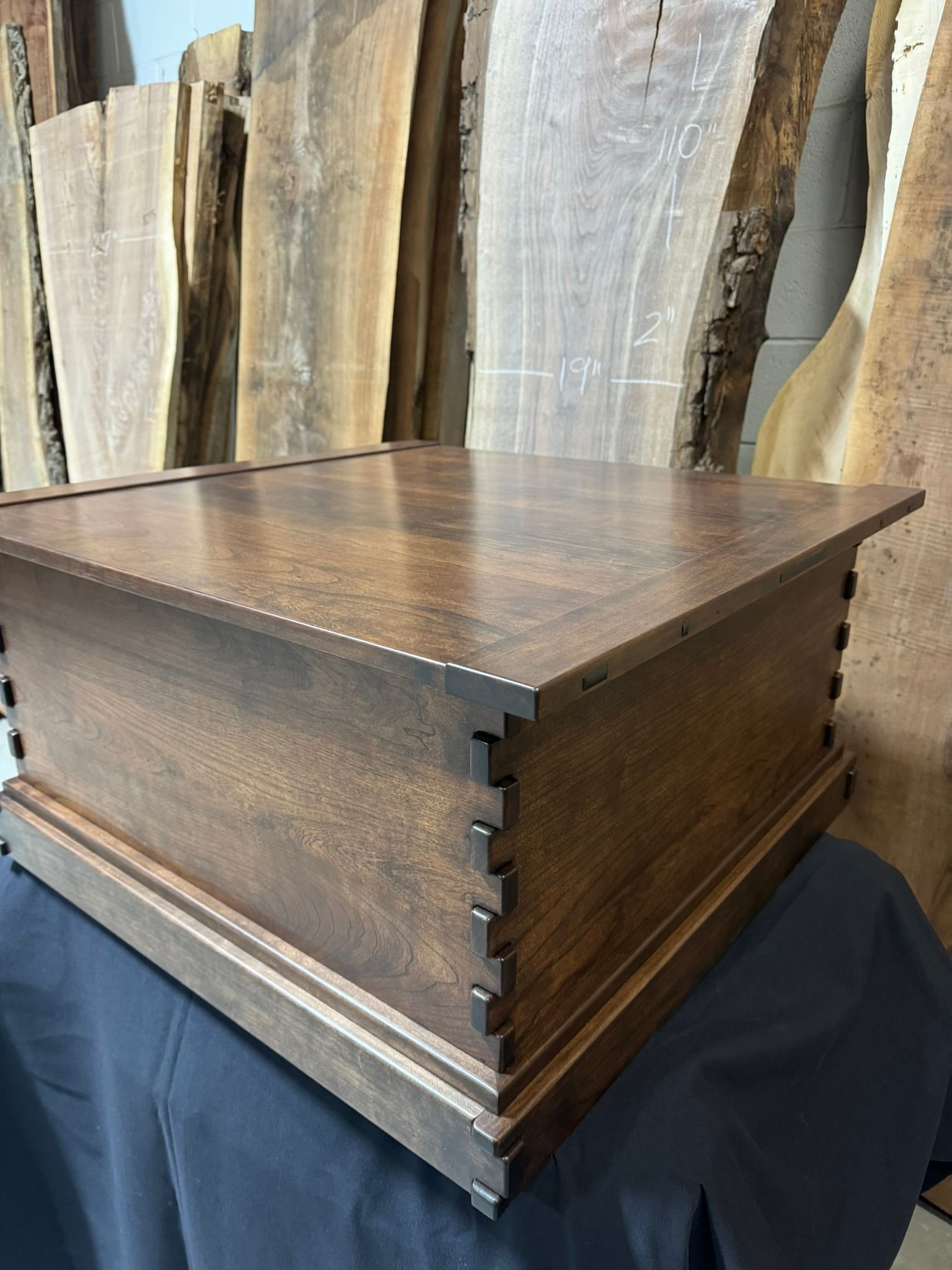 A wooden box is sitting on a table in front of a pile of wood.