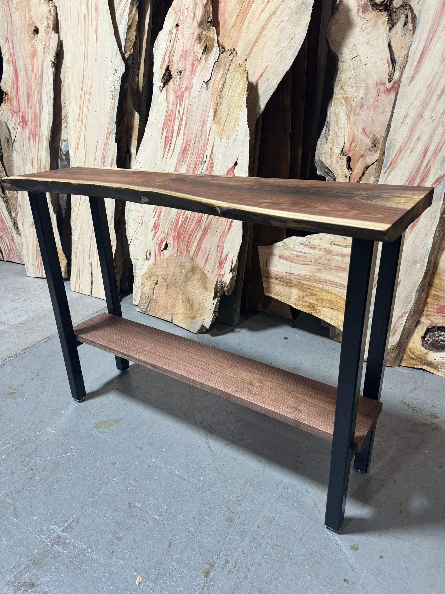 A wooden table with a metal frame and a shelf is sitting on a concrete floor.