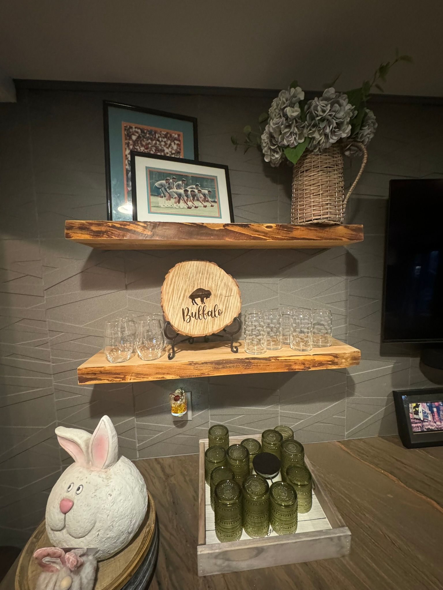 A living room with three wooden shelves , a bunny pillow , and a tray of food.