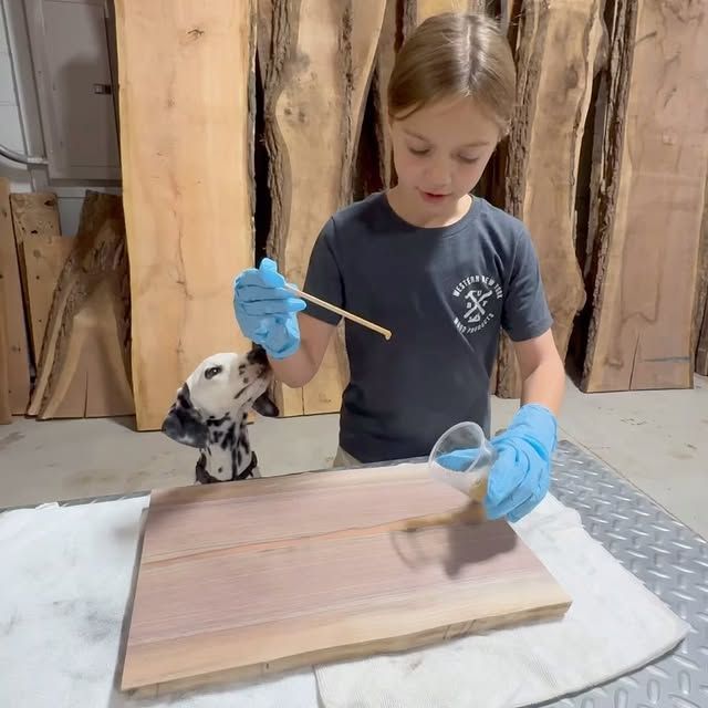 A little girl is painting a piece of wood while a dog watches