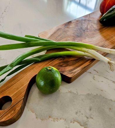 A wooden cutting board with green onions and a lime on it
