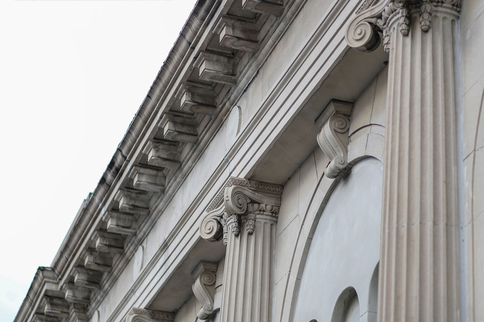 Corinthian columns and ornate frieze on a light-colored building, against a cloudy sky.