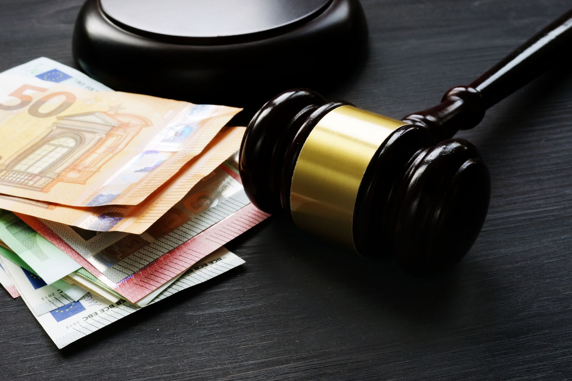Wooden gavel next to a stack of Euro banknotes on a dark surface, potentially representing legal costs.