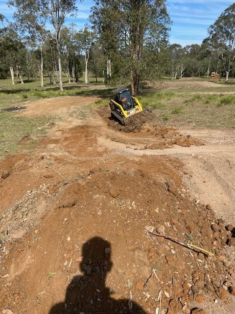 Orange Mini Skid Steer Digging in Dirt — Damon's Earthworks in Chatsworth, QLD