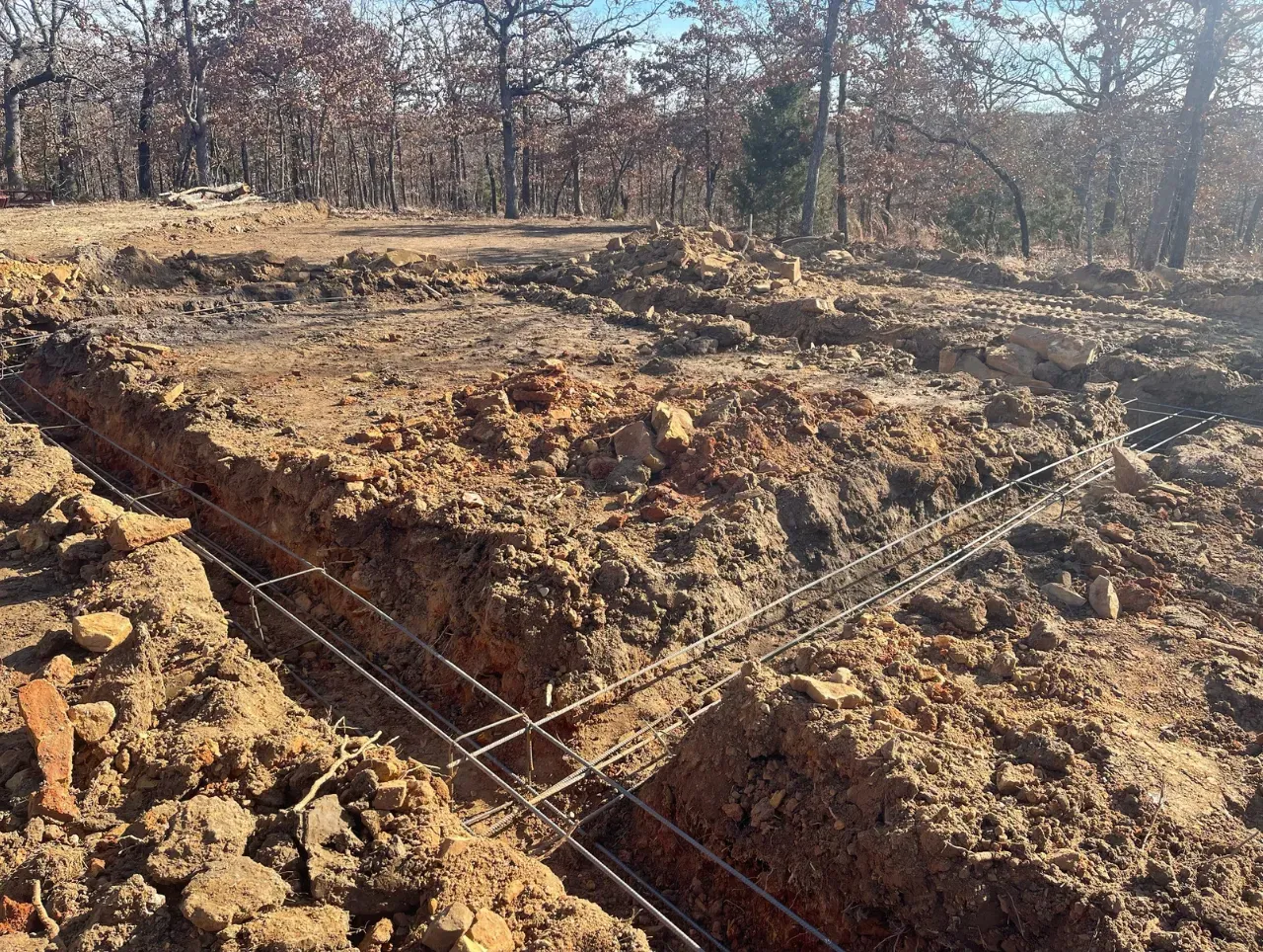 Trenches dug in brown earth with rebar framework, trees in the background.