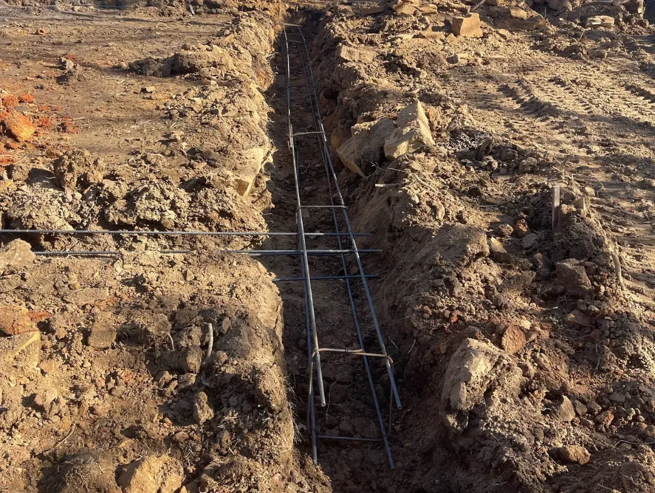 A trench with rebar reinforcement in brown soil, prepared for concrete foundation.