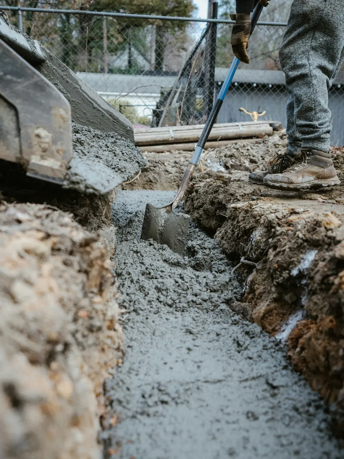 Person shovels wet concrete into a trench from a construction vehicle, outdoors.