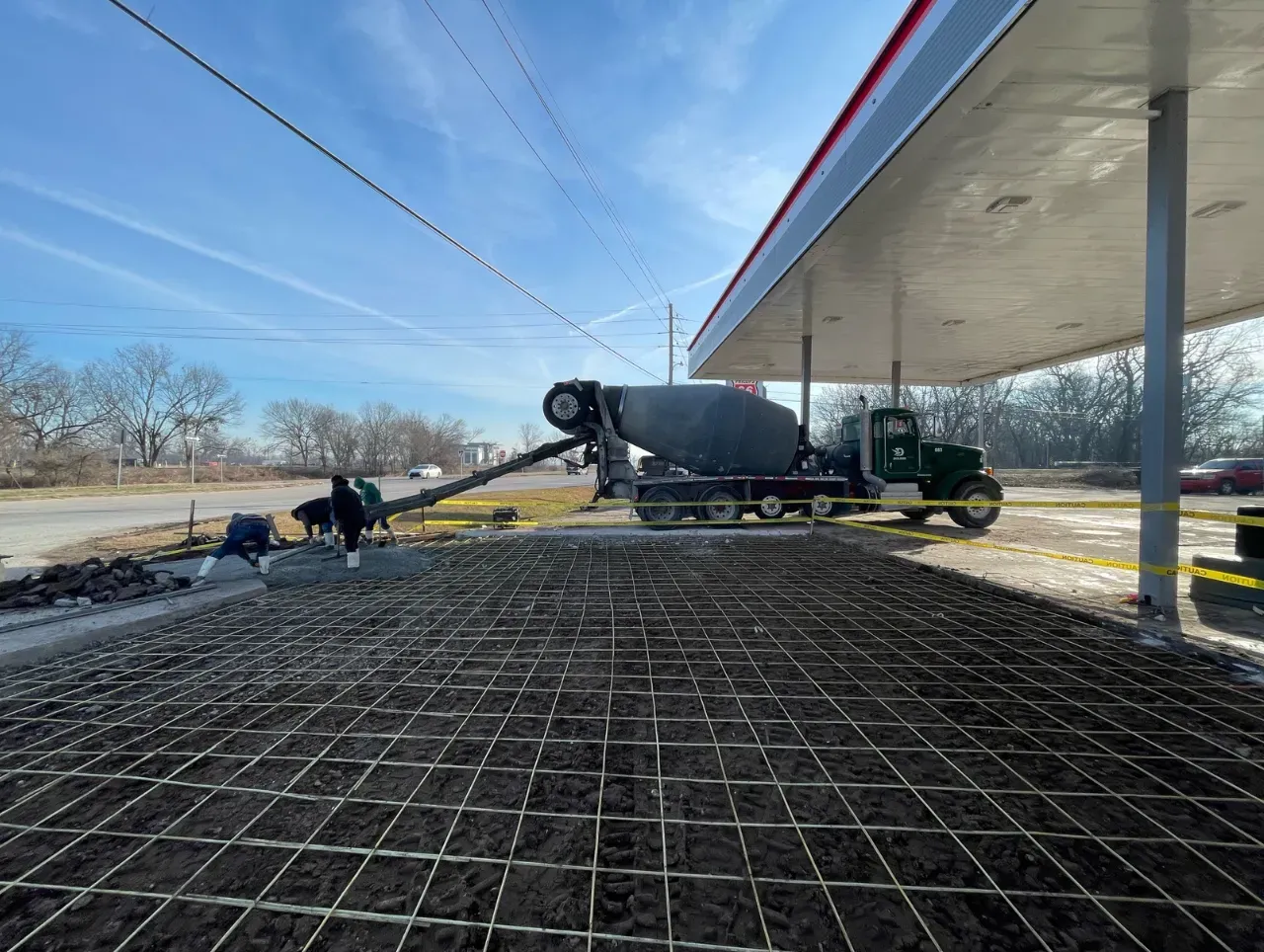 Construction site: Concrete truck pouring concrete onto a rebar grid at a gas station.
