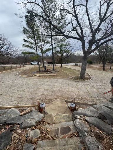 Gravel driveway with a circular turnaround, lined with trees. Gray sky. Stone steps lead up.