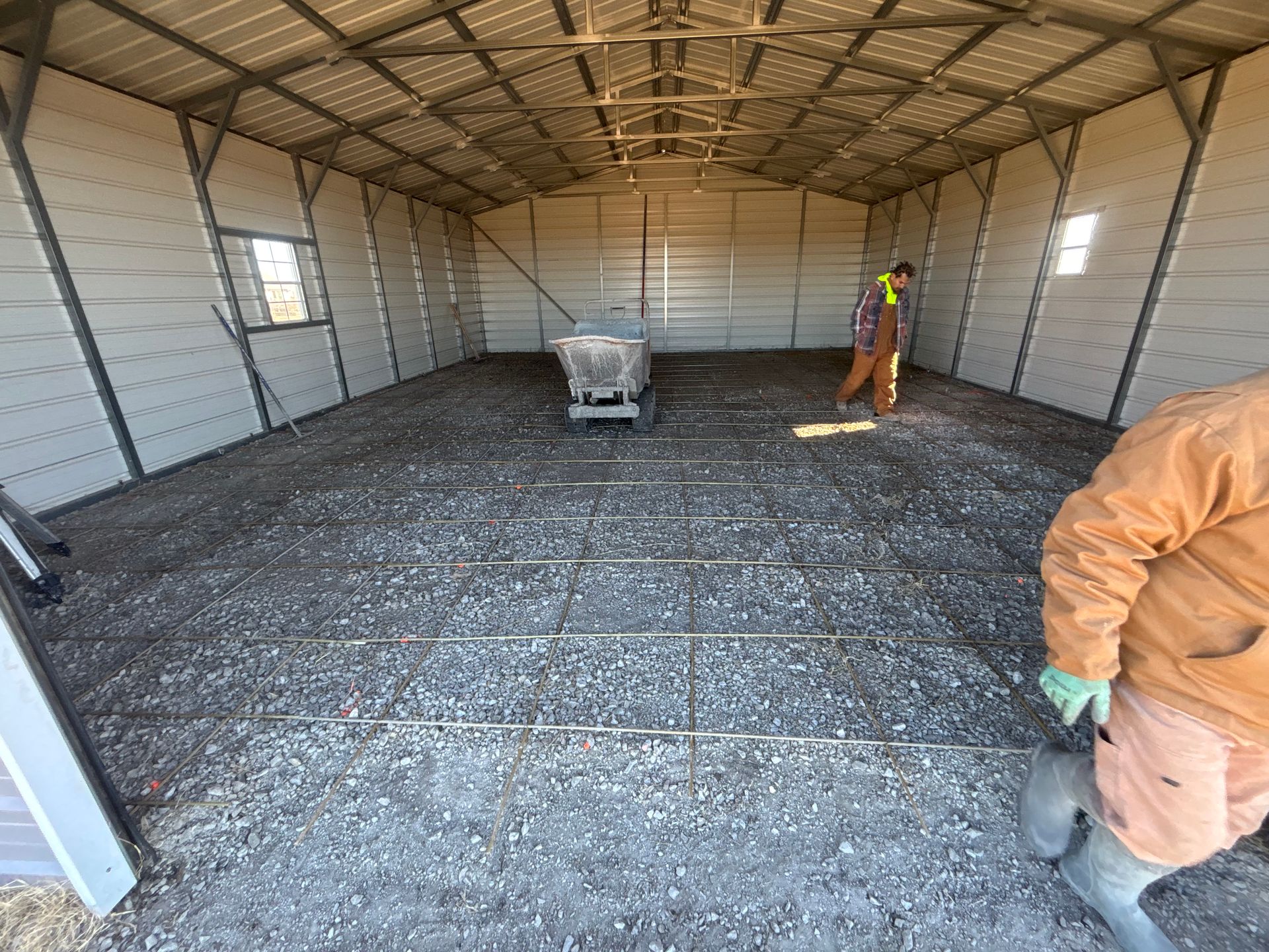 Inside a metal building, workers prepare for concrete flooring, with rebar in place.