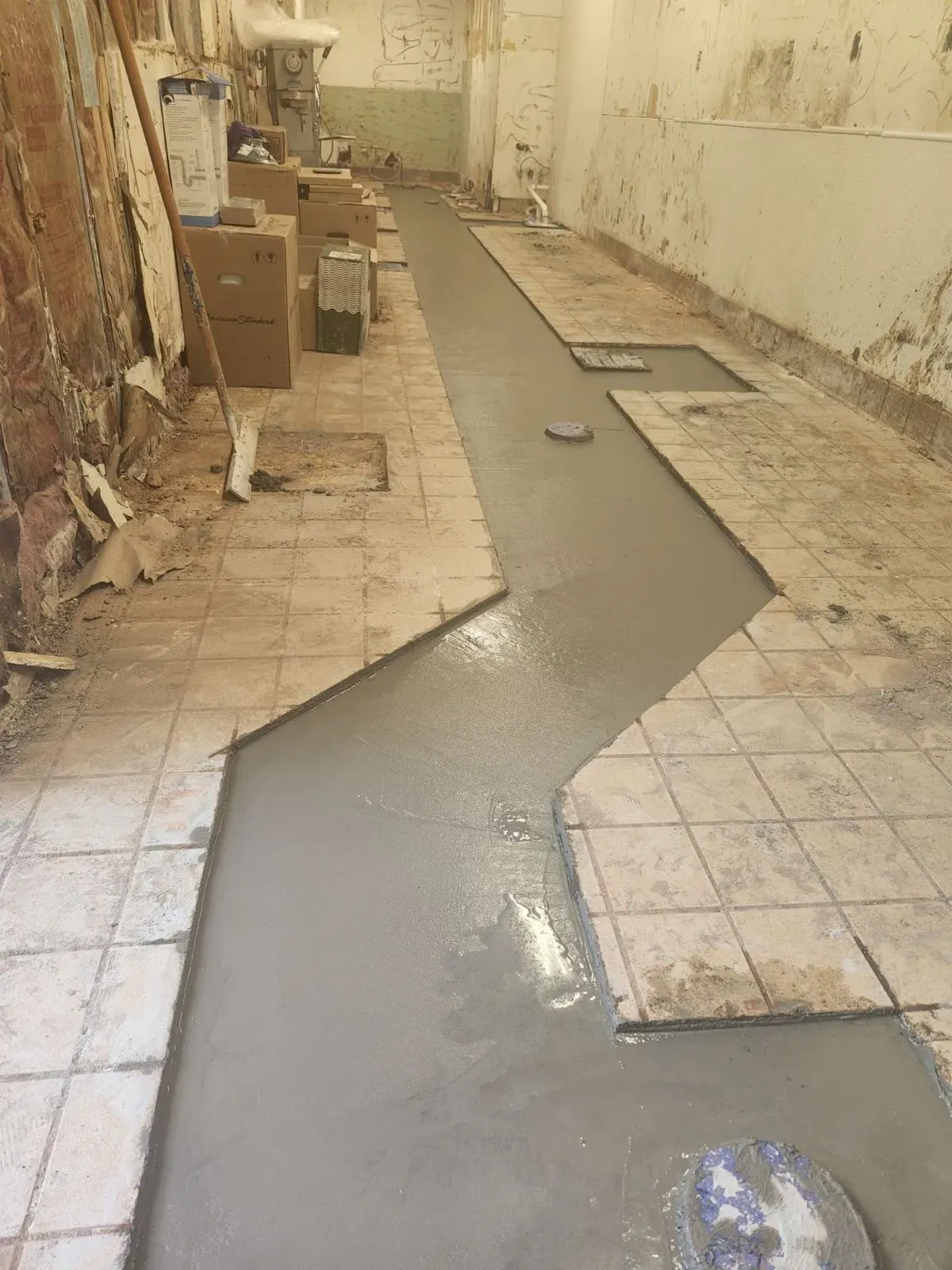 A construction site with new concrete flooring being laid between old tile.