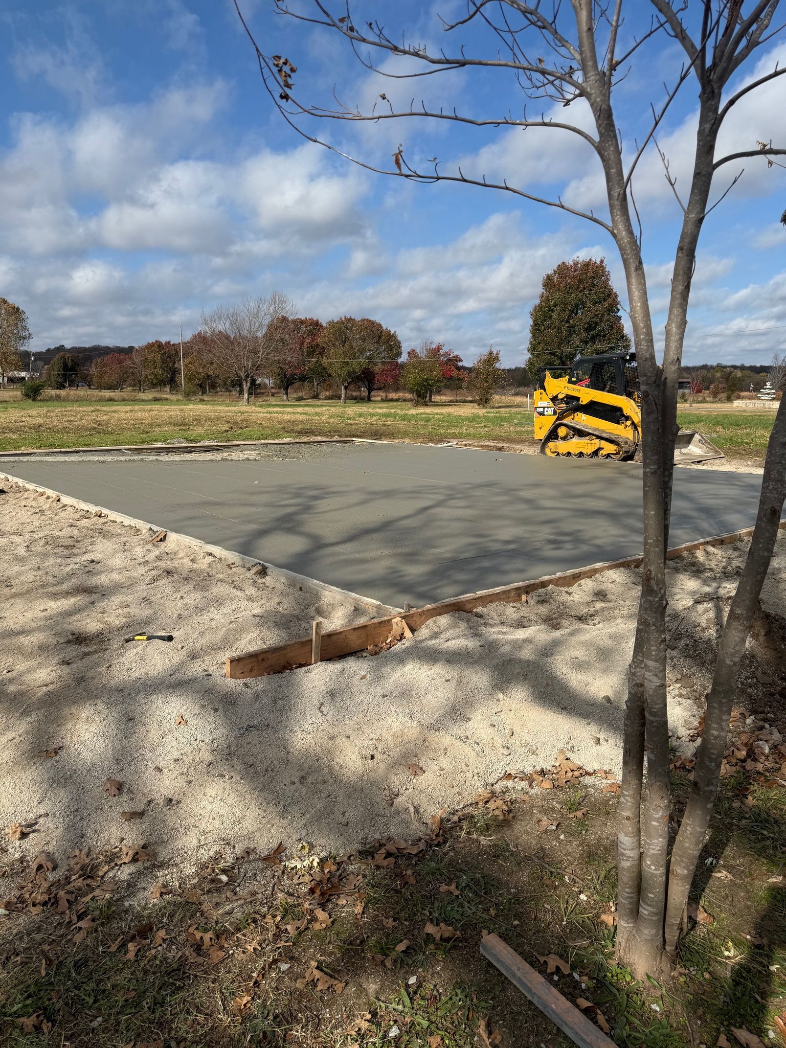 Newly poured concrete slab; gravel border; small tree in the foreground; blue sky and trees in the background.
