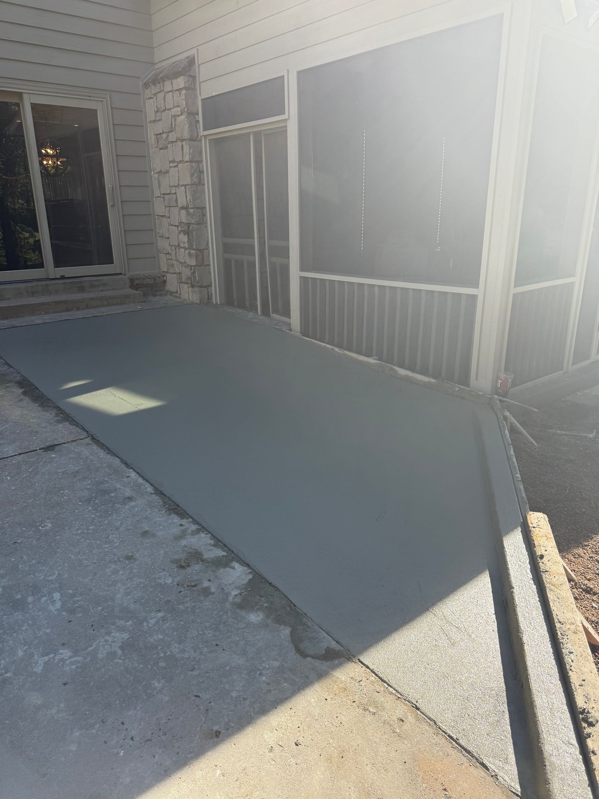Freshly poured concrete ramp leading to a screened porch, next to existing concrete.