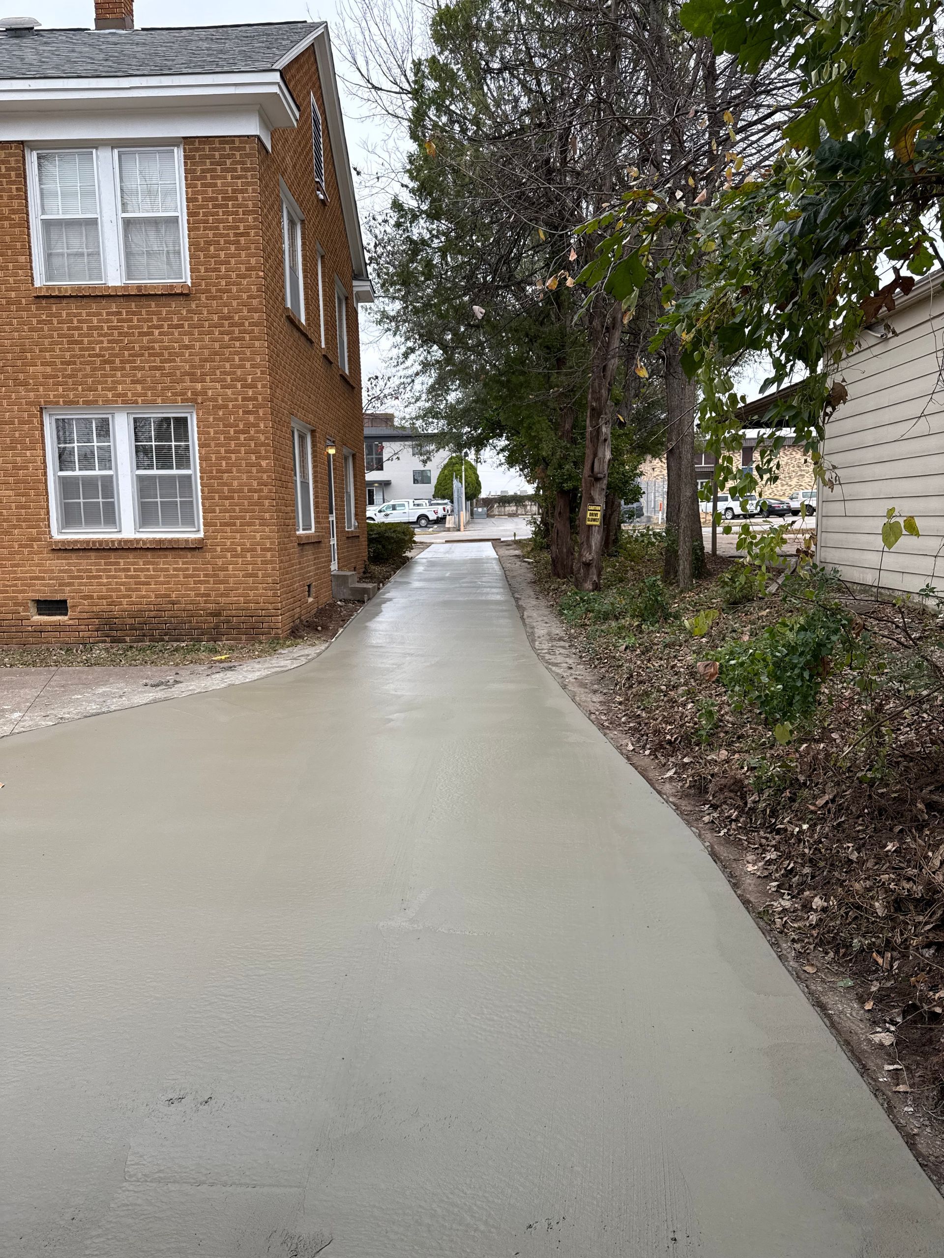 A newly poured concrete alleyway next to a brick building and trees on a cloudy day.