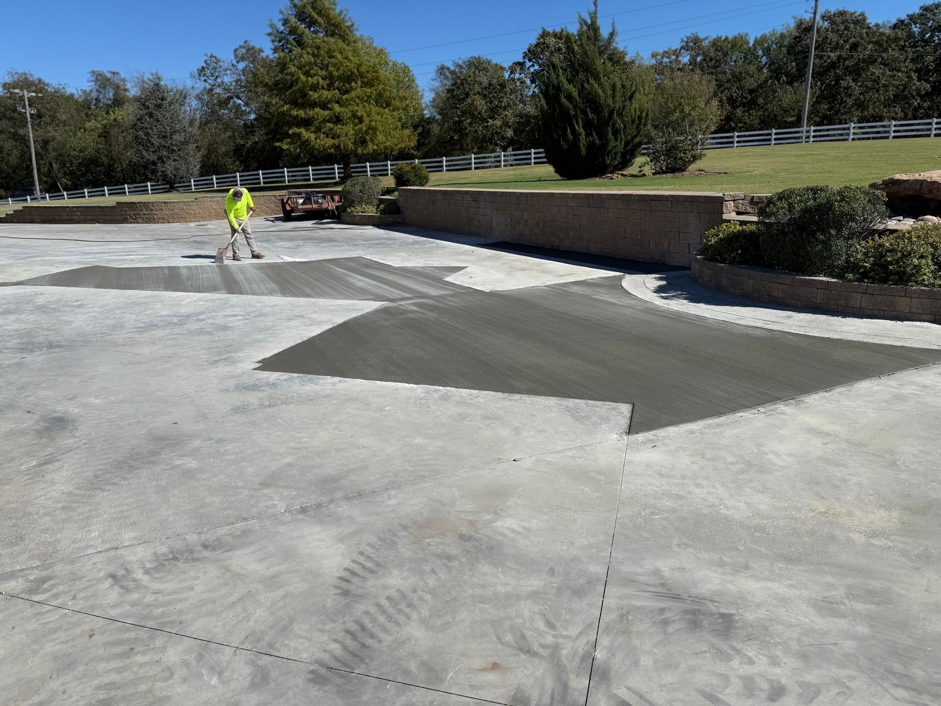 Person in neon vest smoothing wet concrete on a large driveway, near retaining walls and green lawn.