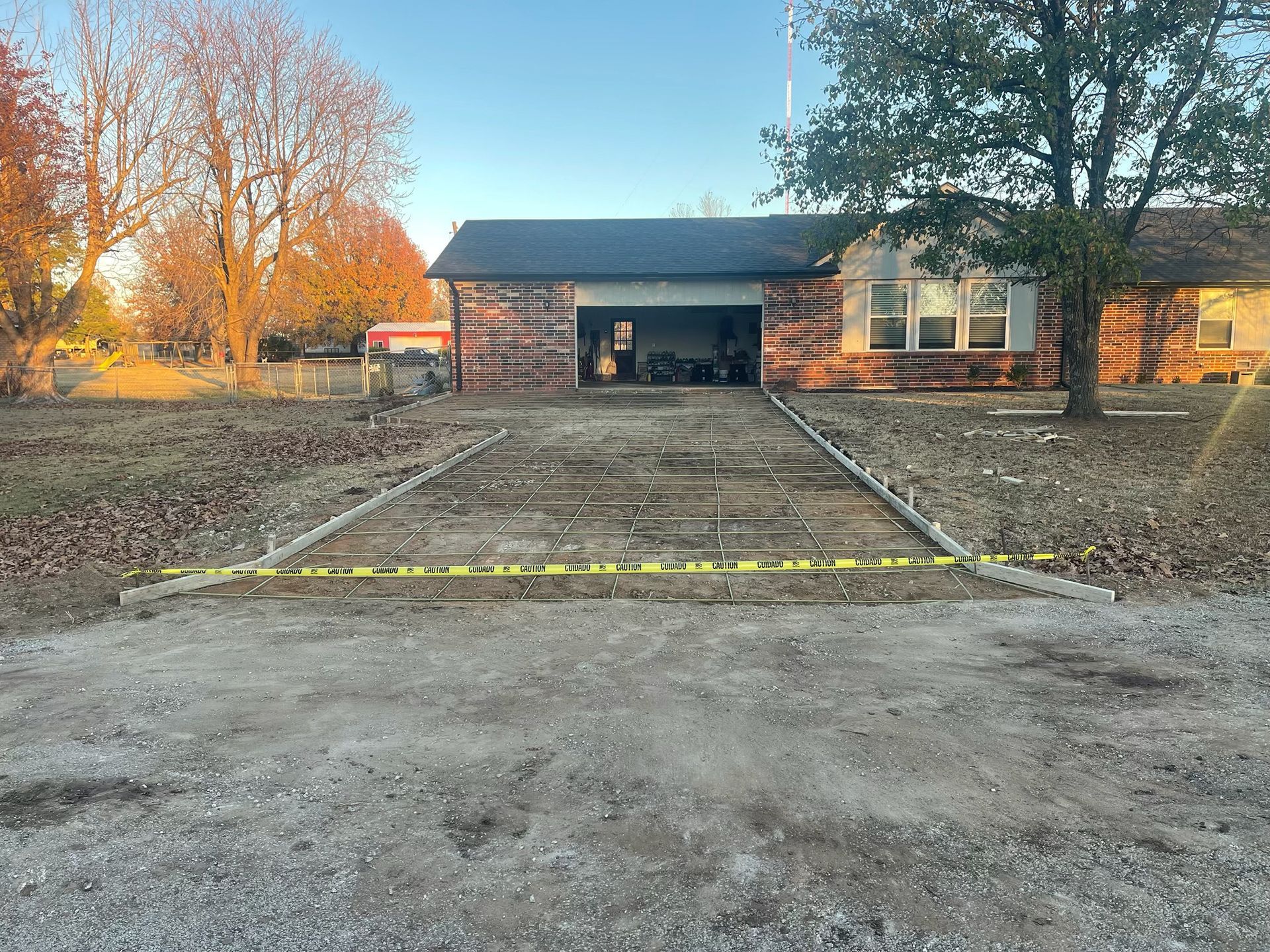 Concrete driveway under construction leading to a house with an open garage. Yellow caution tape blocks access.