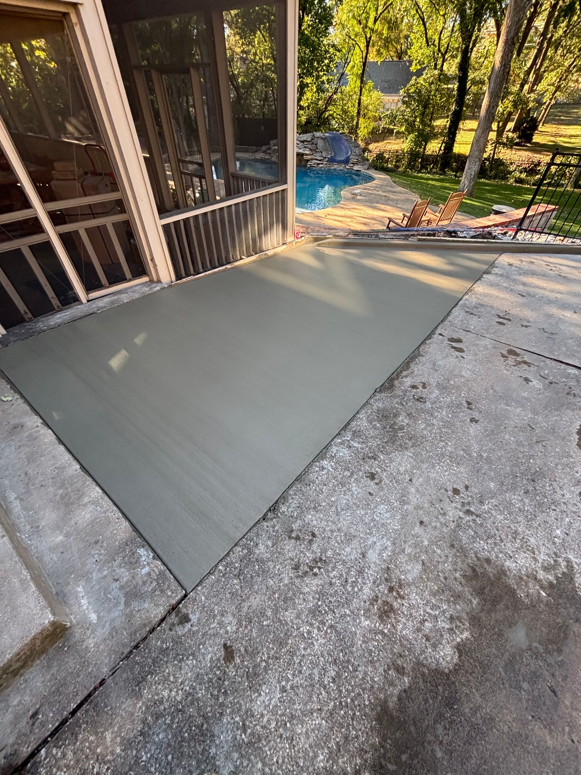 Freshly poured concrete patio next to a screened porch and swimming pool.