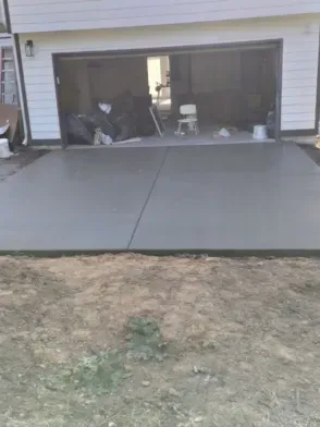 New concrete driveway in front of a garage with open doors; dirt in the foreground.