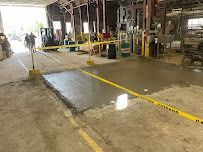 Freshly poured concrete section, marked off with yellow caution tape inside a large industrial building.
