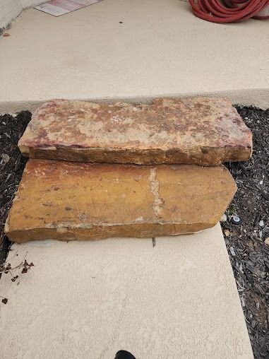 Two weathered stone slabs on a concrete surface. One is on top of the other.