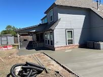 Gray house with new concrete patio and shed under a blue sky.