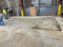 Workers removing concrete section of floor in industrial building.