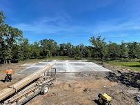 Construction site with a concrete foundation, a trailer, and a sunny blue sky.