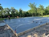 Freshly poured concrete foundation, wooden frame, with pipes, in a grassy area with trees and blue sky.